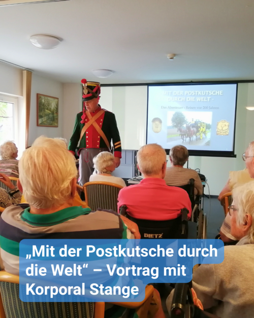 Eine Gruppe voller Senioren lauscht, dem Vortrag eines kostümierten Redners. Er trägt eine rot-schwarze Uniform. Bildunterschrift: „Mit der Postkutsche durch die Welt“ – Vortrag mit Korporal Stange